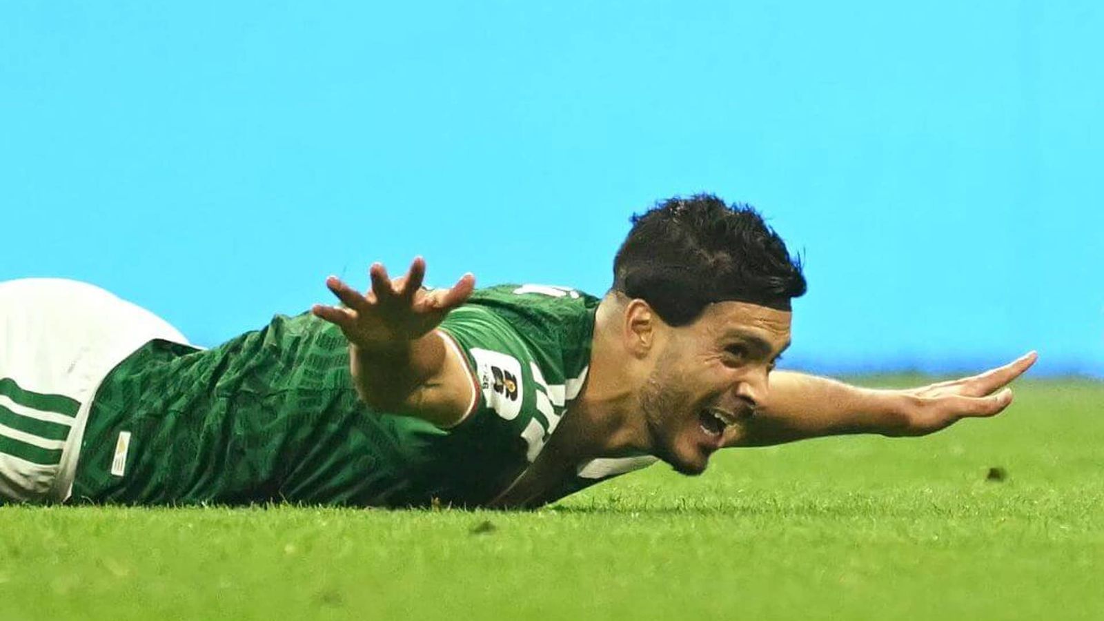 A soccer player in a green jersey sliding on the grass celebrating a goal