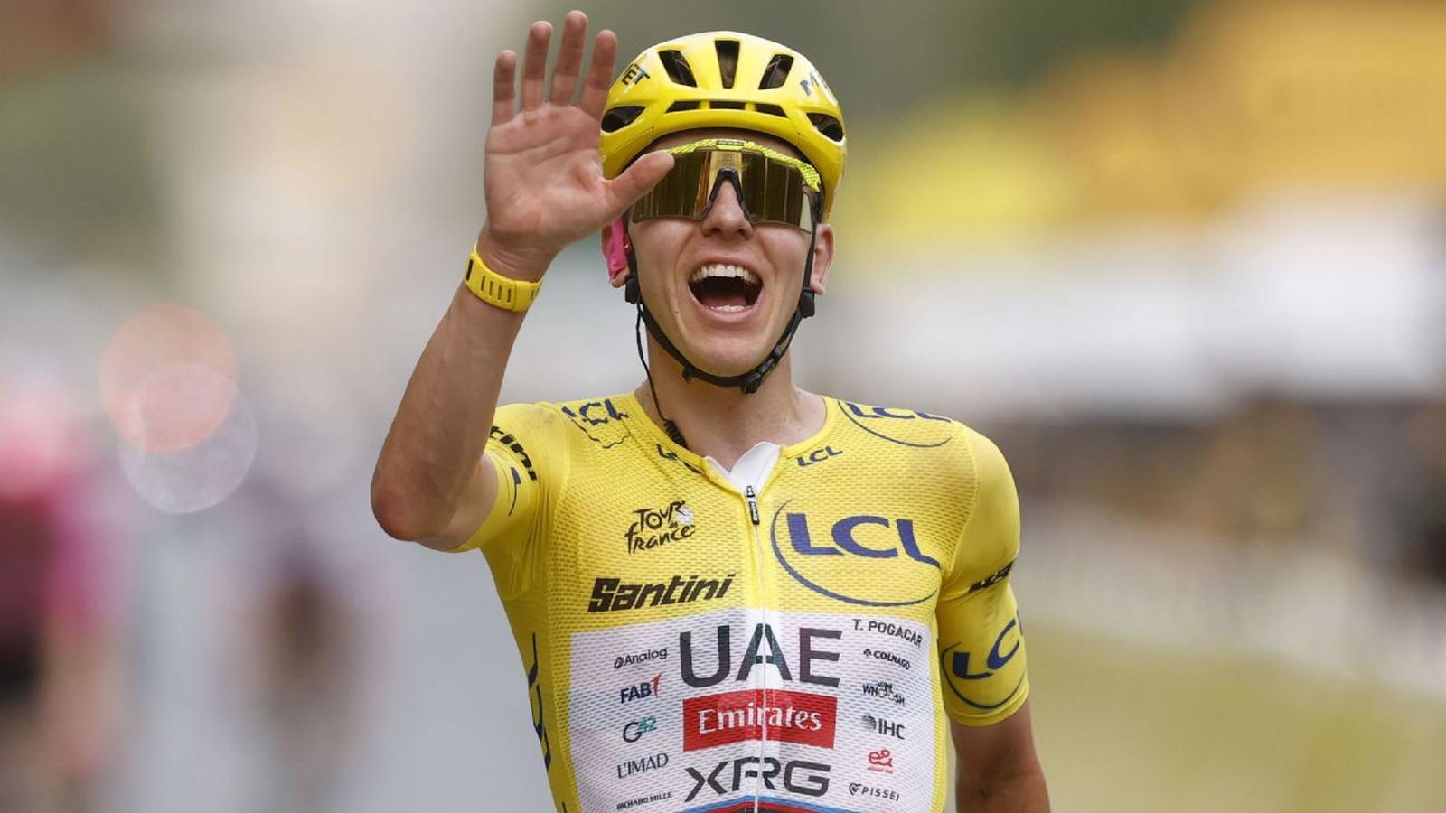 Tadej Pogačar wearing the yellow jersey and helmet waving to the crowd