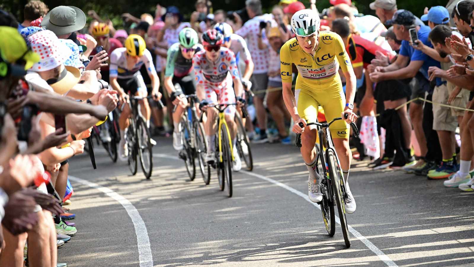 Tadej Pogačar wearing the yellow jersey cycling uphill surrounded by cheering spectators