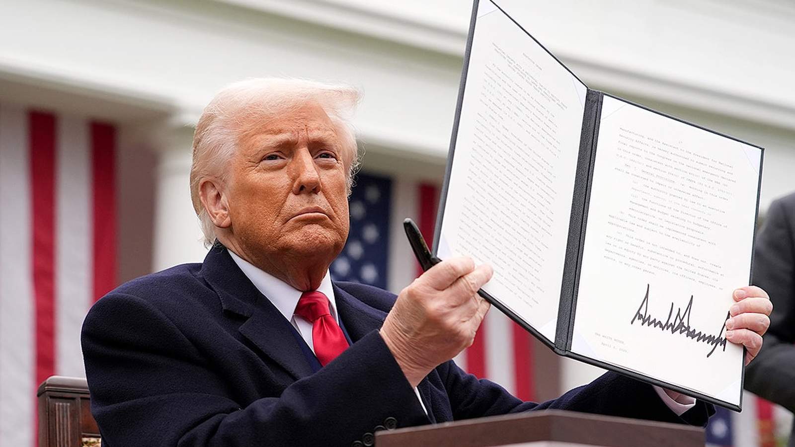 Donald Trump holding up a signed executive order document at a White House event
