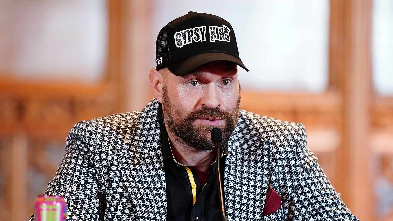 Tyson Fury wearing a Gypsy King cap and patterned blazer at a press conference