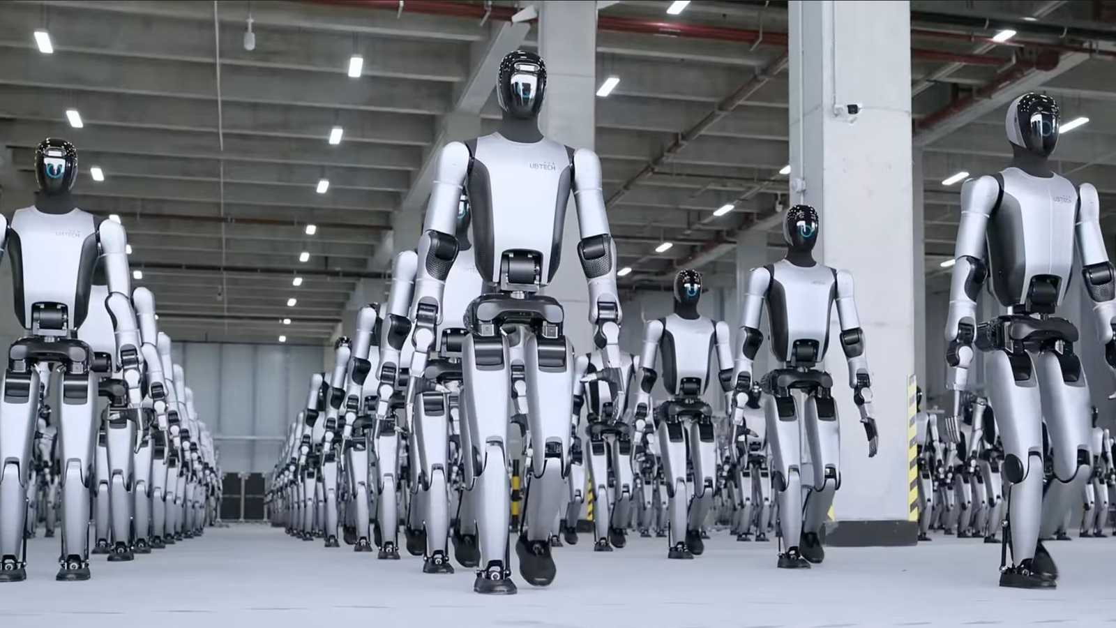 Multiple silver and black Ubtech humanoid robots walking in a factory setting