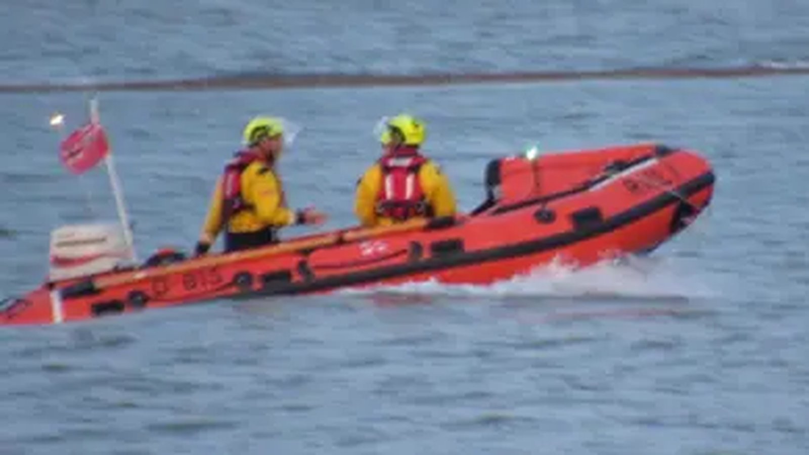 Two lifeboat crew members in yellow gear on an orange inflatable rescue boat