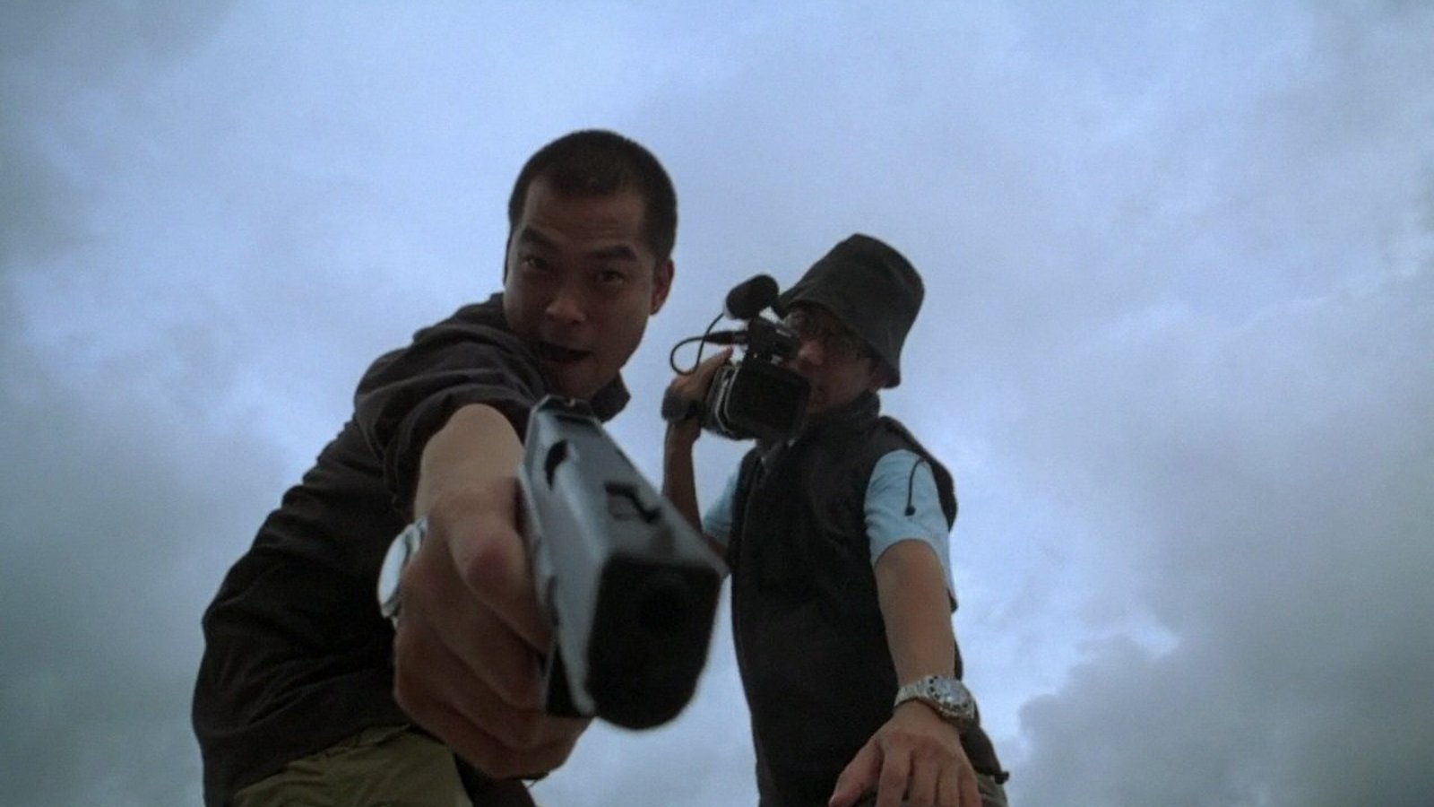 A man points a handgun at the camera while a cameraman films him