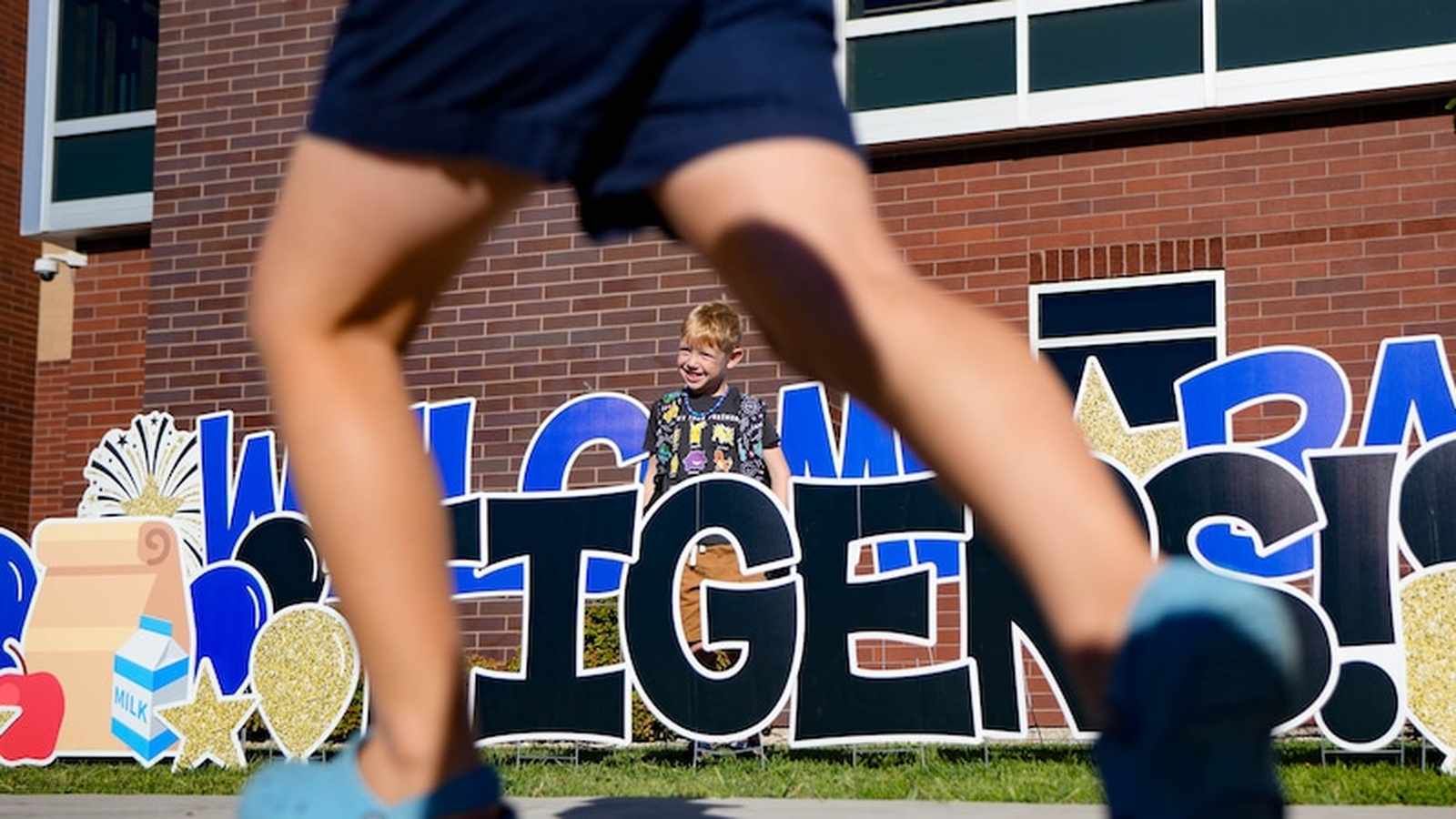A young student stands behind a welcome back sign at an Alpine school