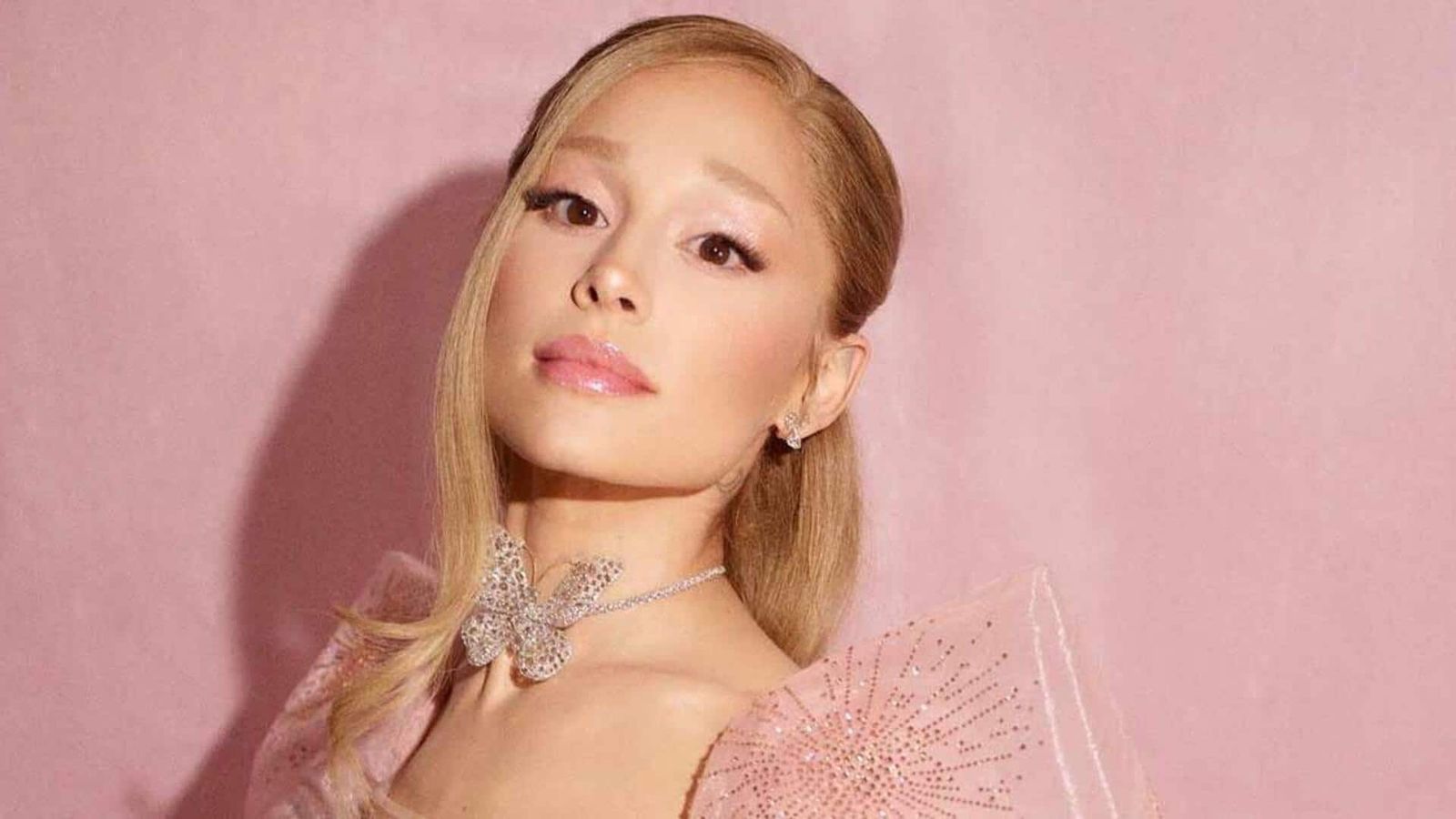 Ariana Grande posing in a pink outfit with a butterfly necklace