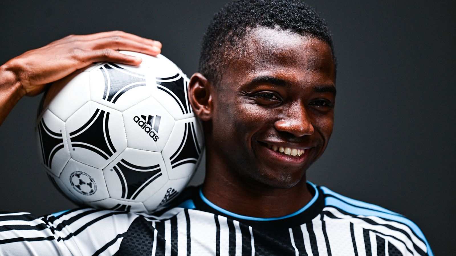 Ivorian winger Bazoumana Toure smiling while holding an Adidas soccer ball in studio
