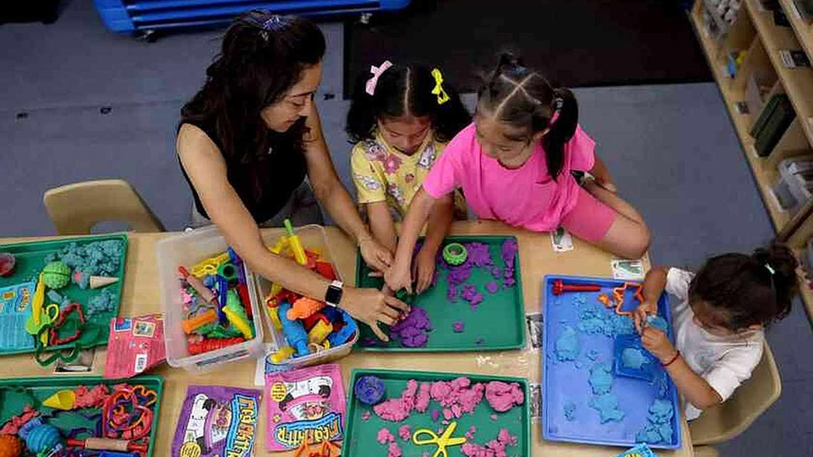 A teacher and three young children playing with colorful modeling clay at classroom tables