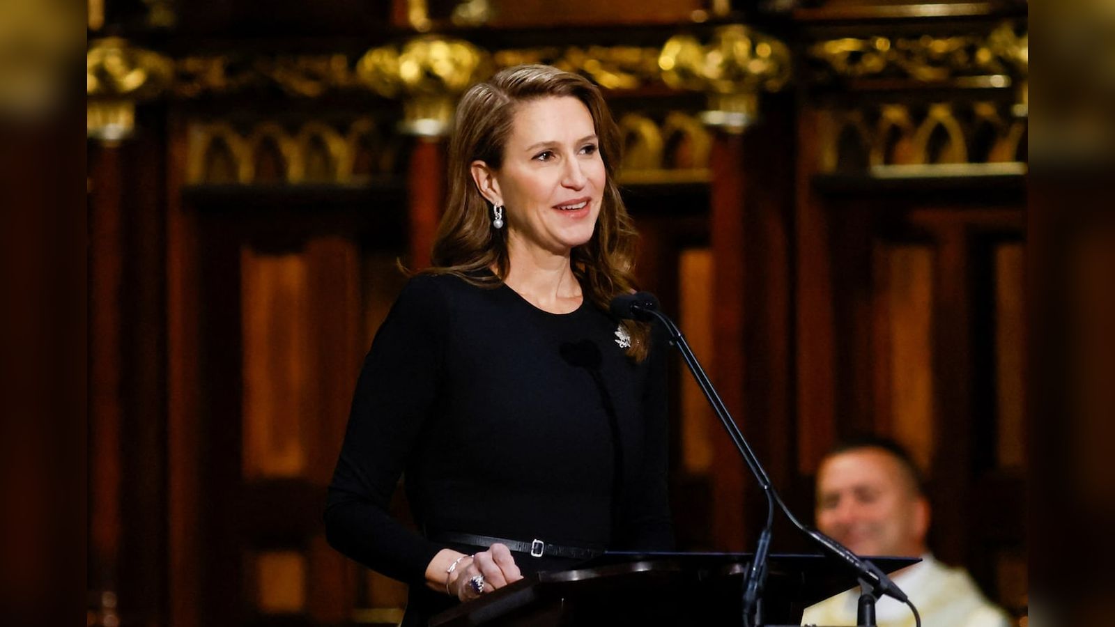 Caroline Mulroney wearing a black dress speaking at a wooden podium indoors