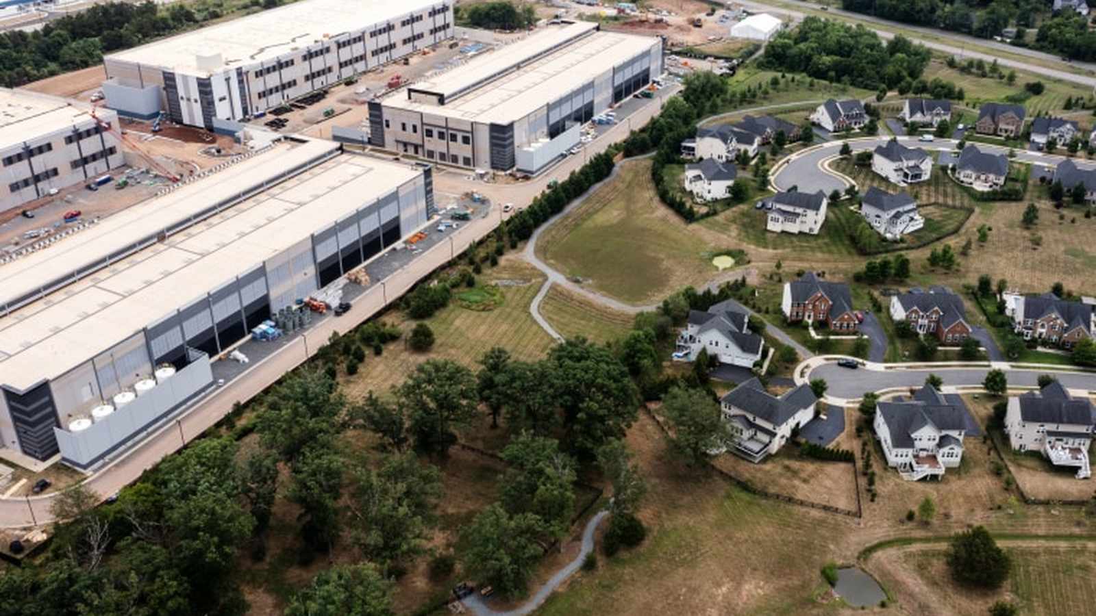 Aerial view of large industrial data center buildings situated next to a suburban neighborhood