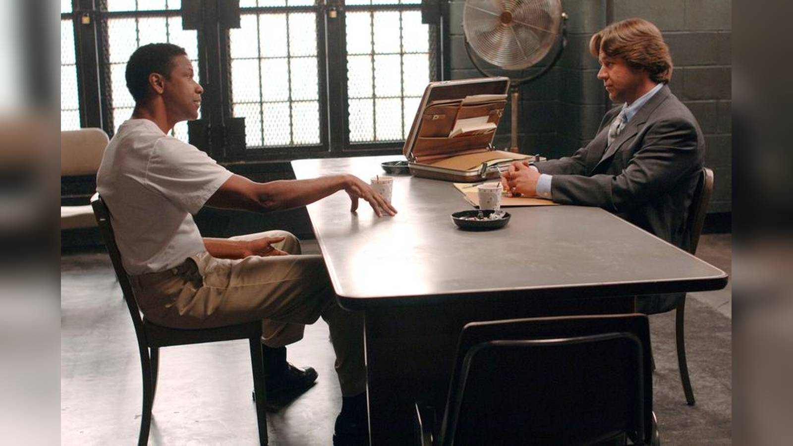Denzel Washington and Russell Crowe sit across from each other at a table