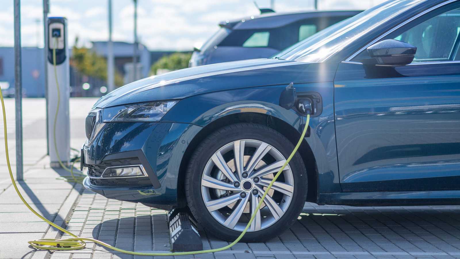 A blue electric car parked and charging at a public charging station outdoors