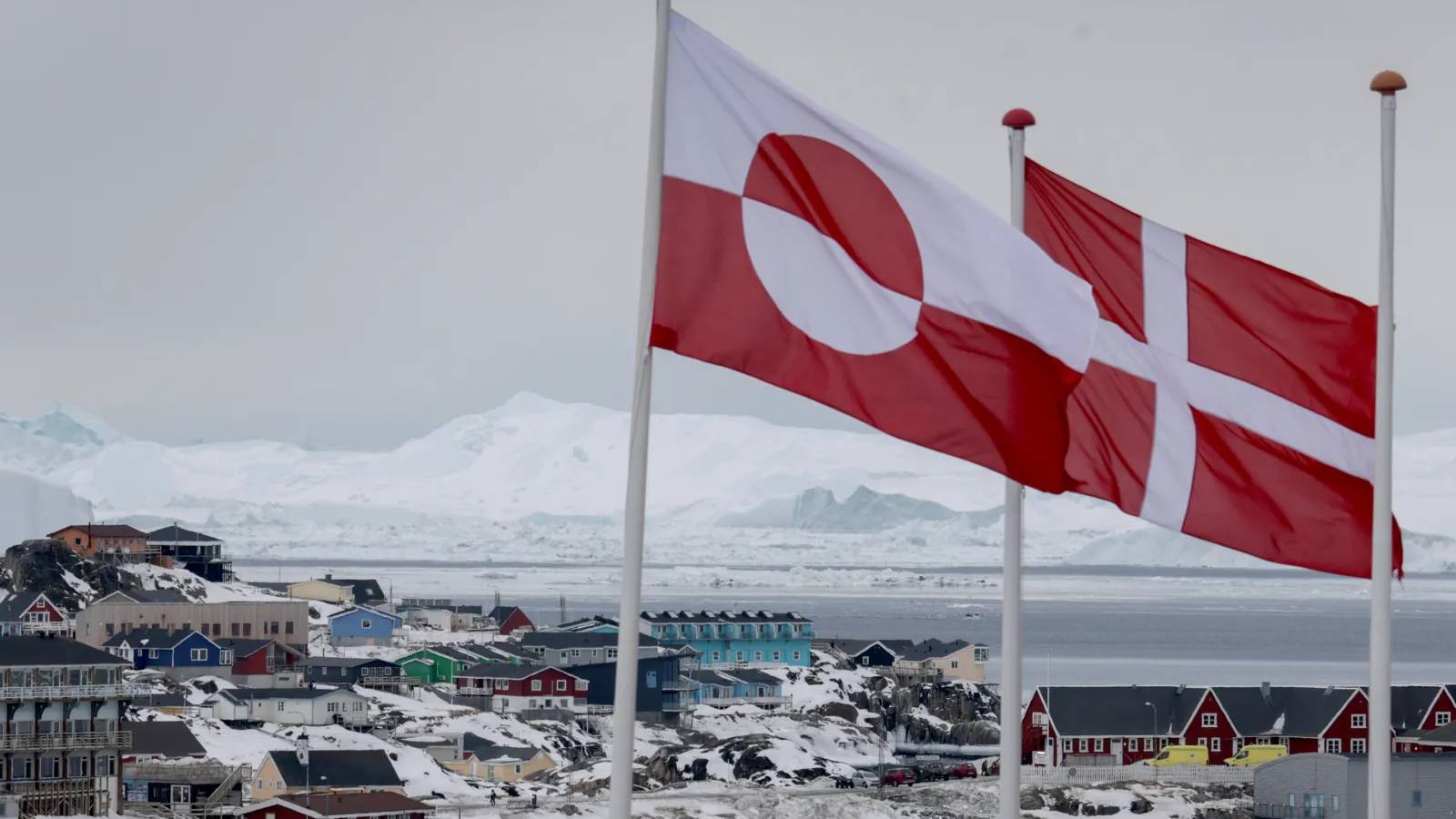 The flags of Greenland and Denmark flying over a snowy coastal town in Greenland