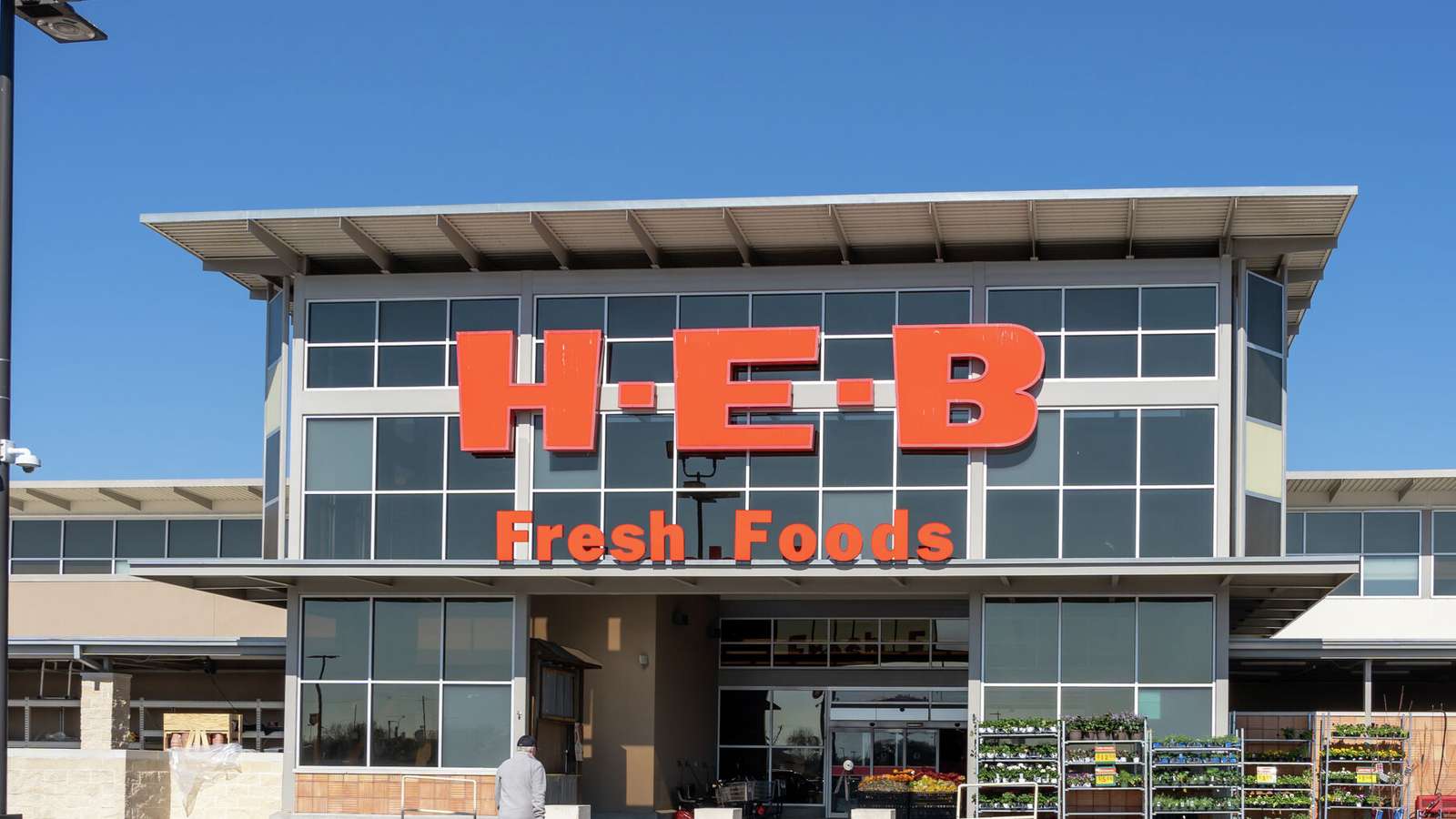 The exterior entrance of an H-E-B grocery store with large orange signage on a sunny day