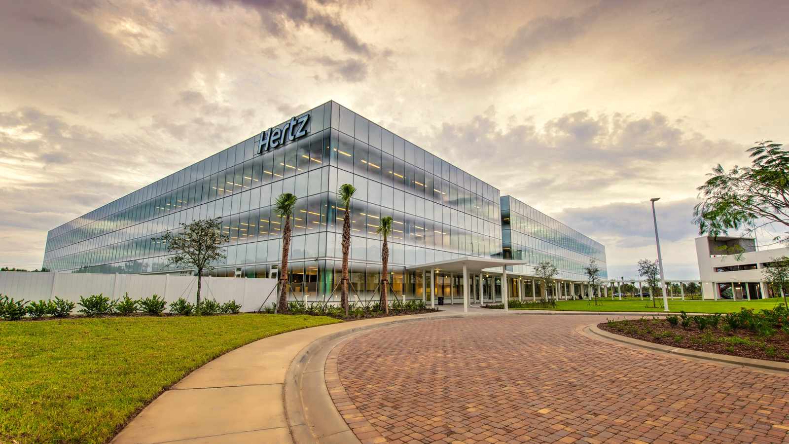 Modern glass exterior of the Hertz corporate headquarters building under a cloudy sky