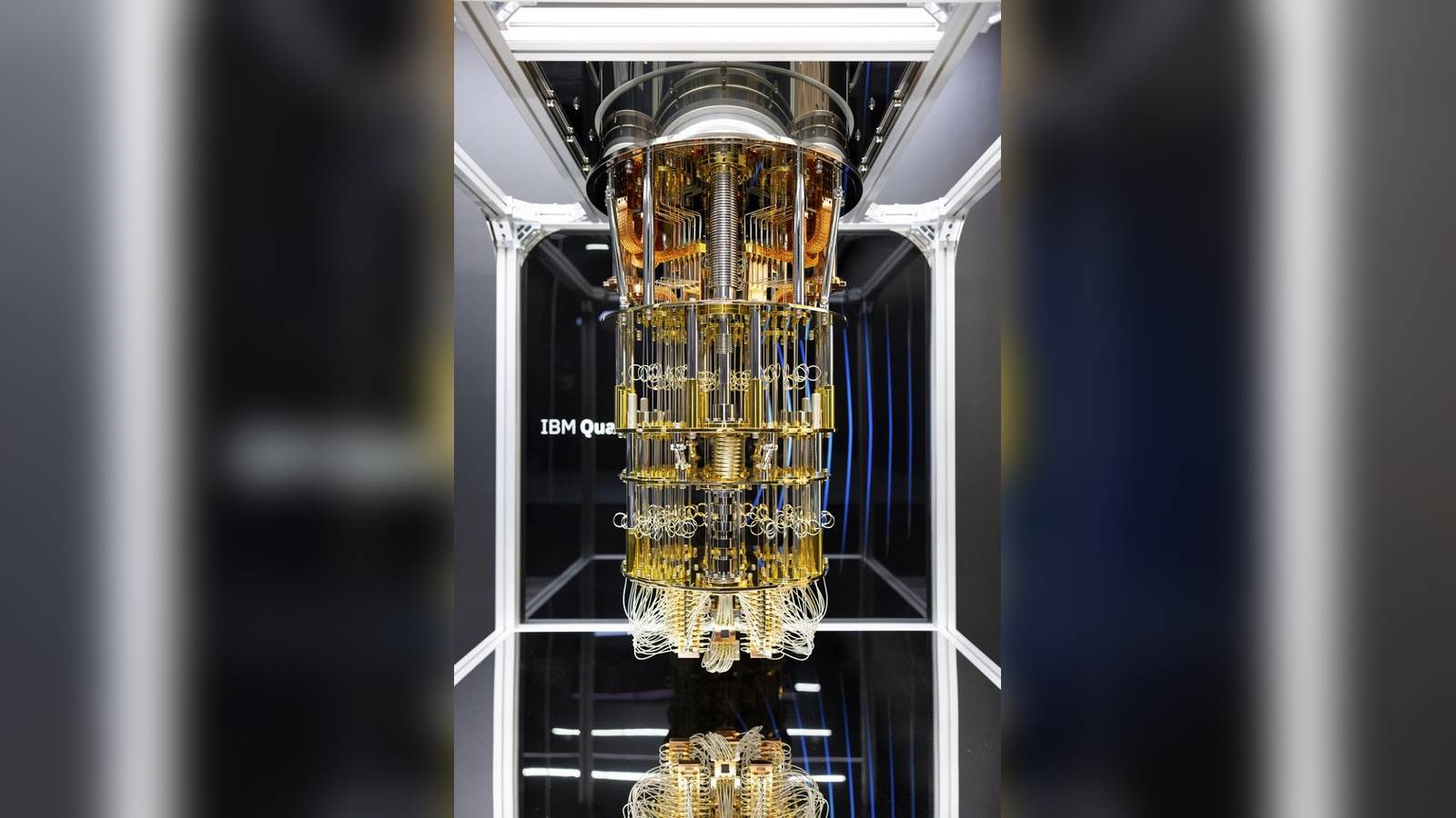 A gold and silver IBM quantum computer processor suspended inside a glass display case