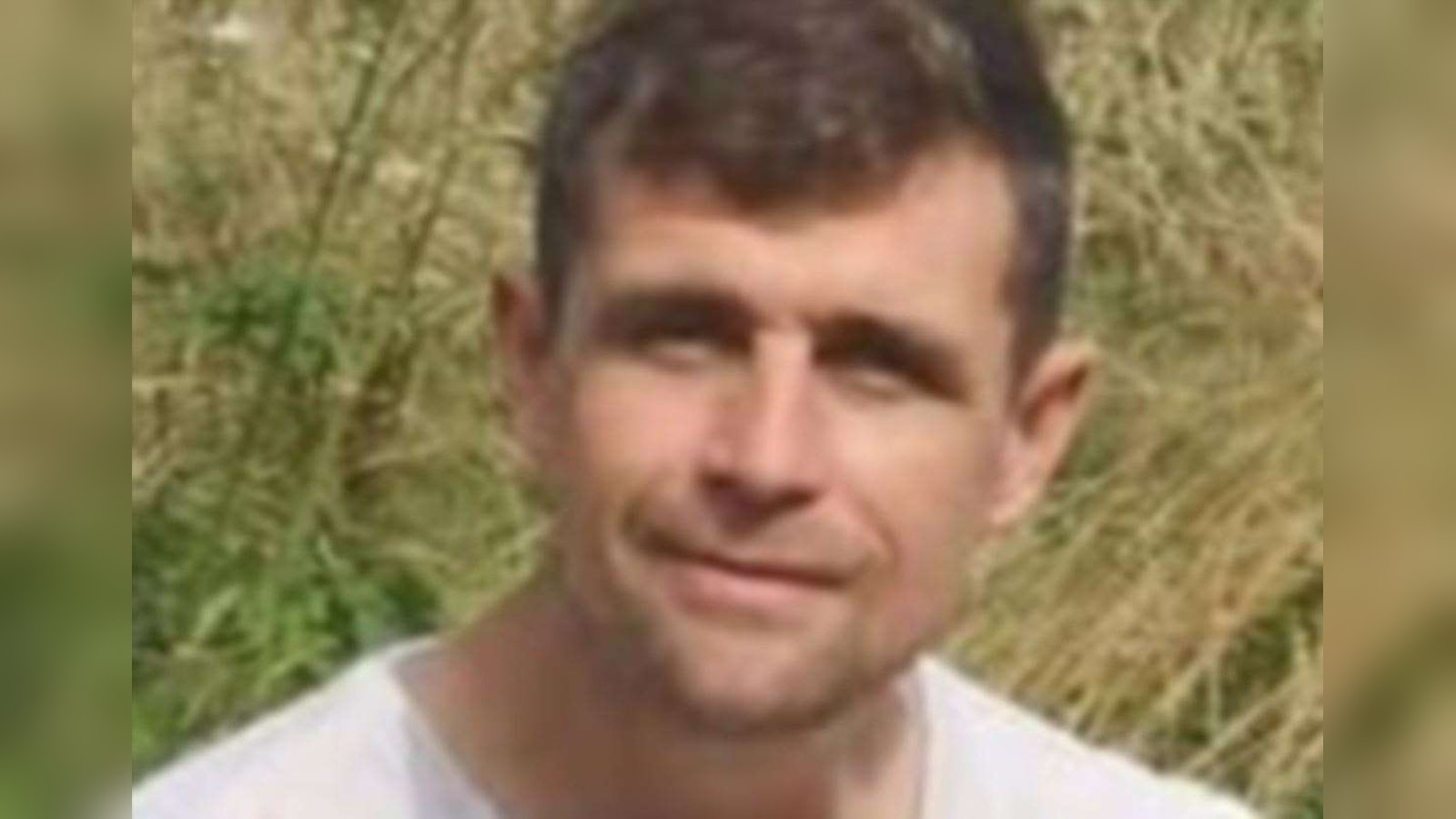 A portrait of a man with short brown hair wearing a white shirt