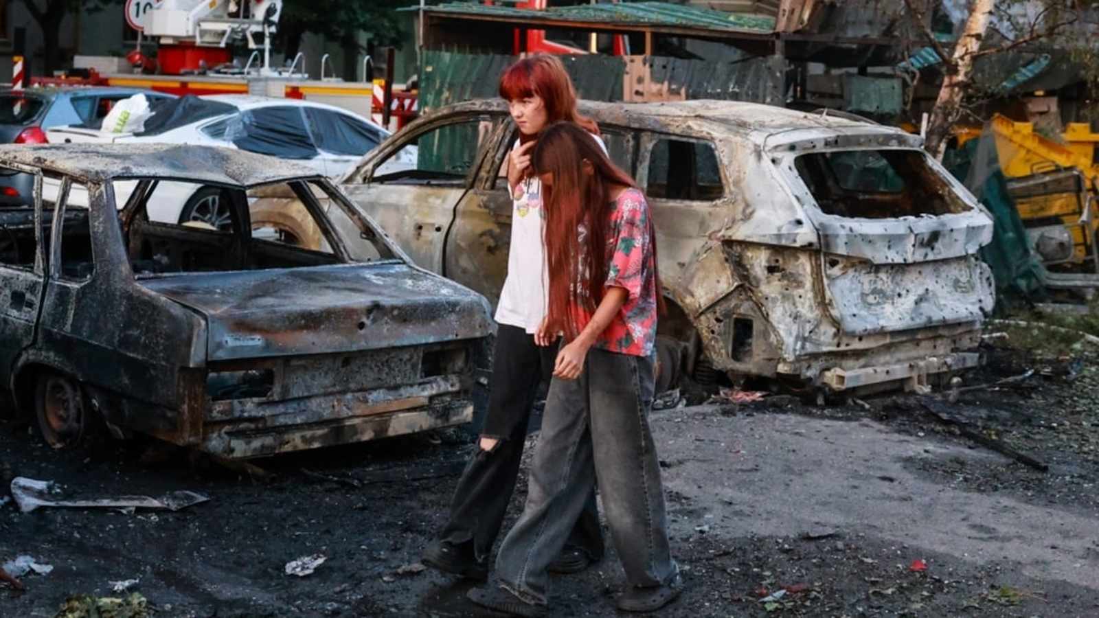 Two young women walking past destroyed and burnt cars after a missile attack in Kyiv