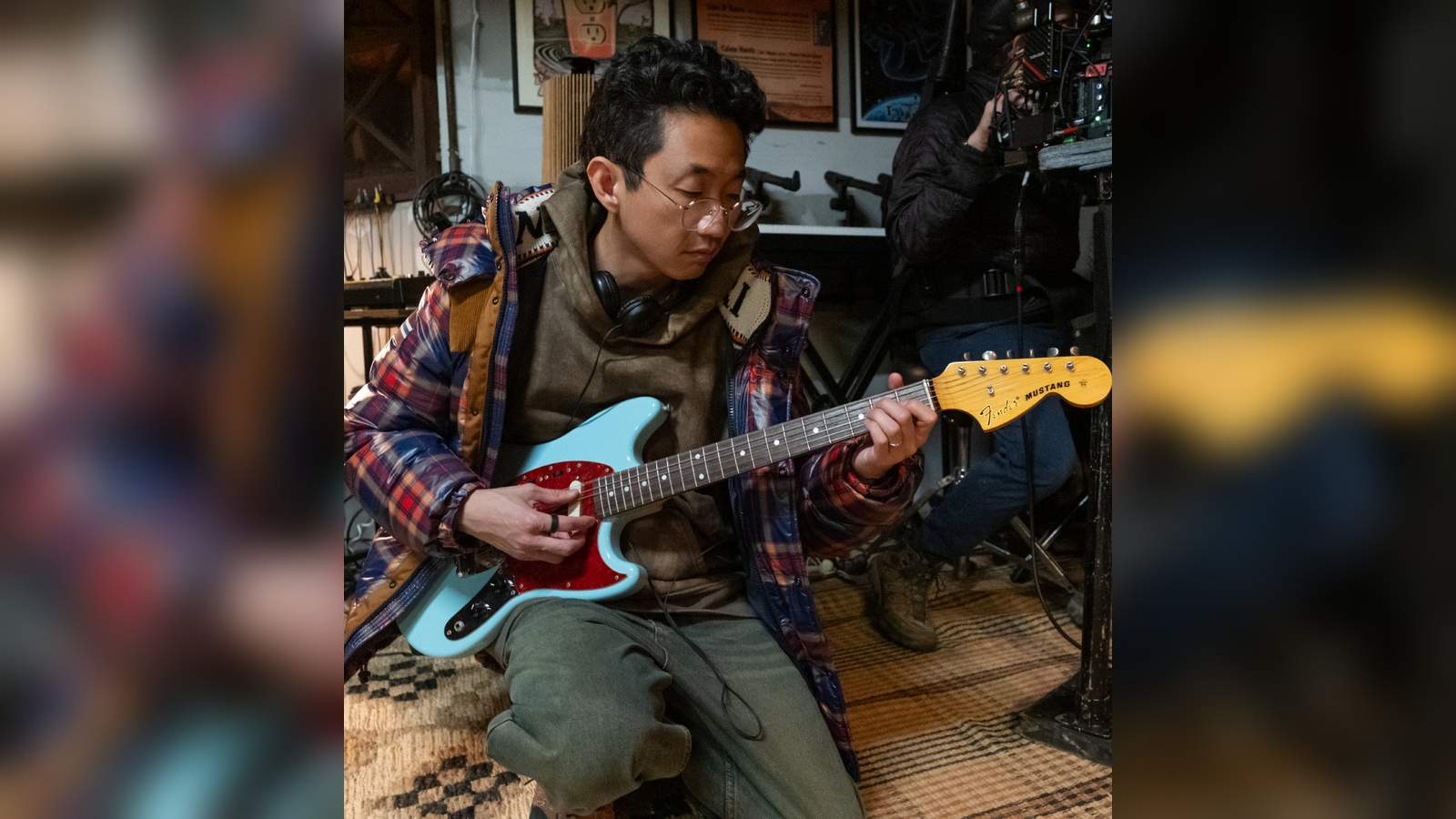 Beef creator Lee Sung Jin playing a light blue Fender Mustang electric guitar indoors