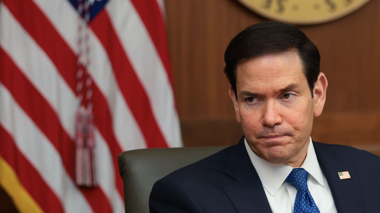 Secretary of State Marco Rubio sitting in front of an American flag background