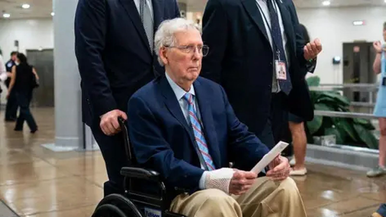Senator Mitch McConnell sitting in a wheelchair while wearing a suit and medical bandage