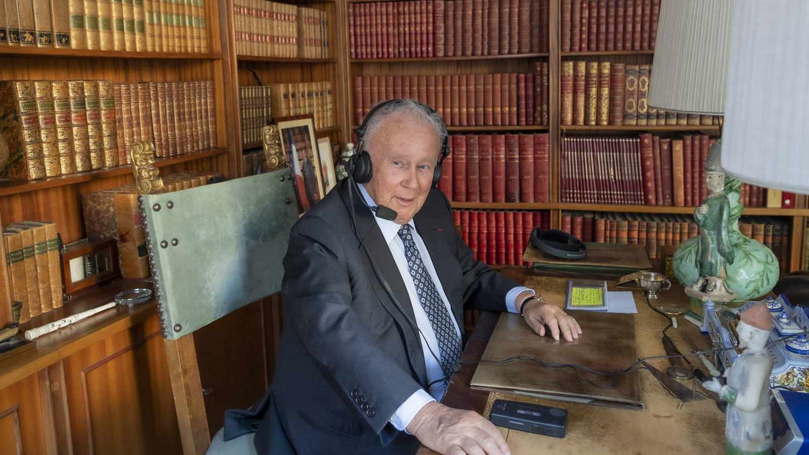 French journalist Philippe Bouvard wearing headphones while sitting at his desk in his library