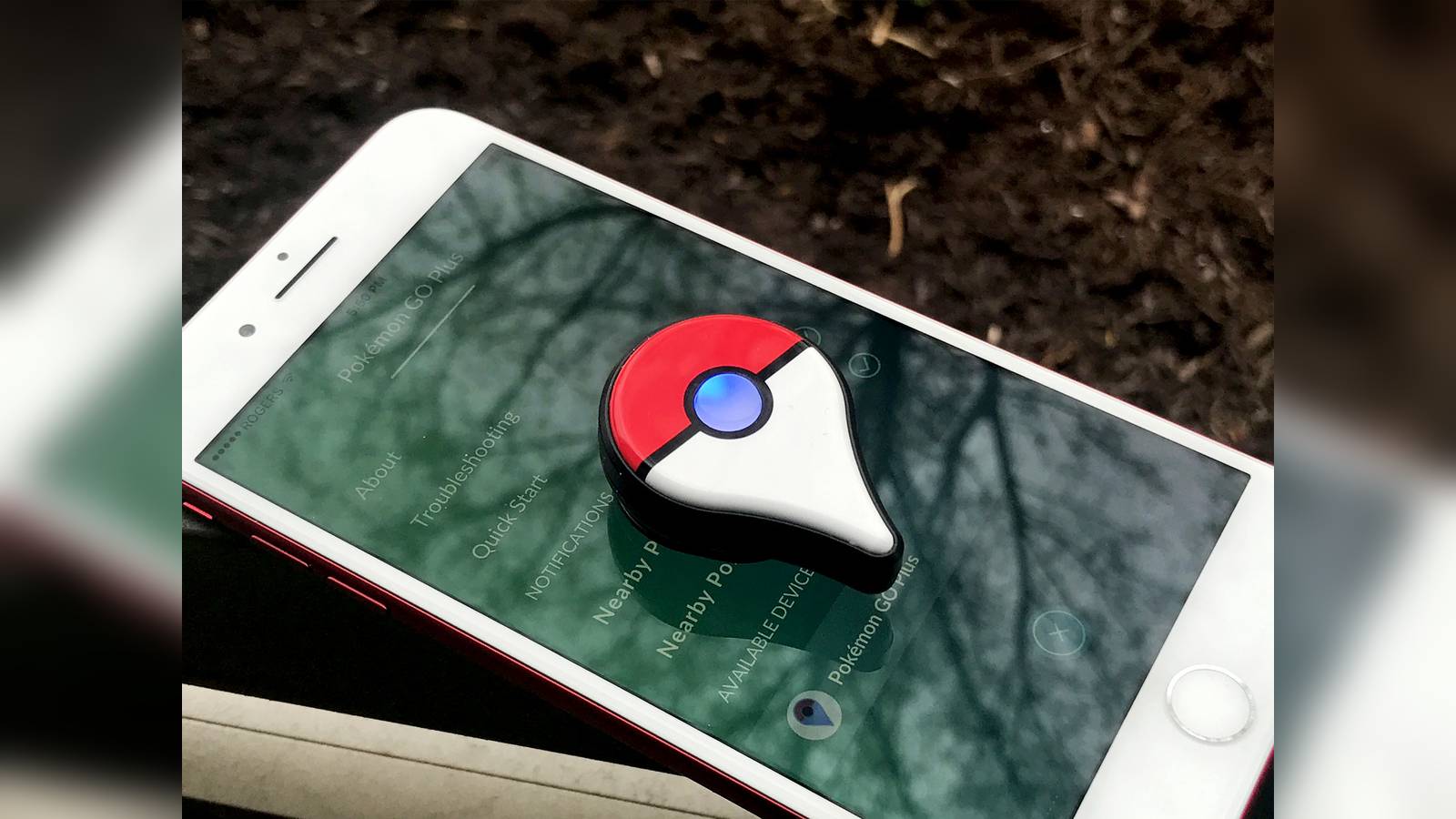 A Pokemon GO Plus accessory resting on a smartphone screen displaying app settings