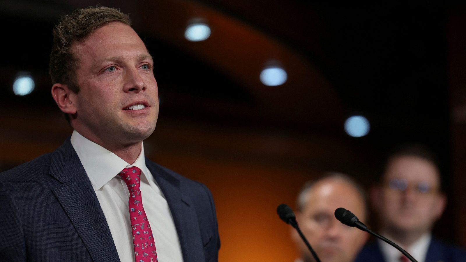Representative Max Miller speaking at a press conference in a dark room