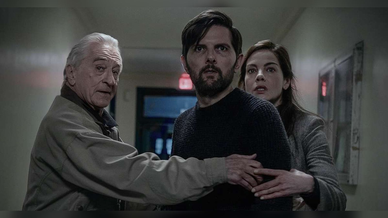 Robert De Niro, Adam Scott, and Michelle Monaghan looking concerned in a dimly lit hallway