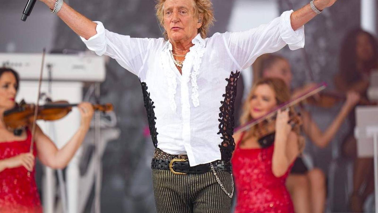 Rod Stewart performing on stage with his band in a white shirt