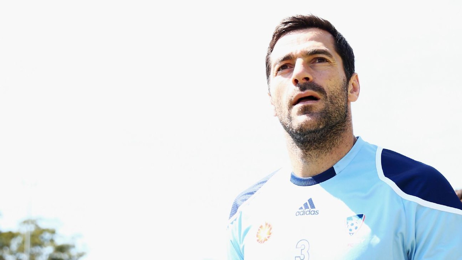 Sasa Ognenovski looking upwards while wearing a light blue soccer training jersey