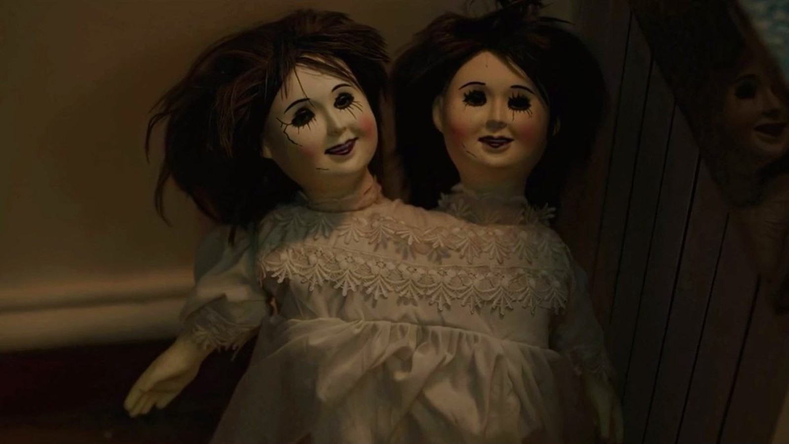 Two vintage-style porcelain dolls with dark hair and white dresses sitting together in darkness