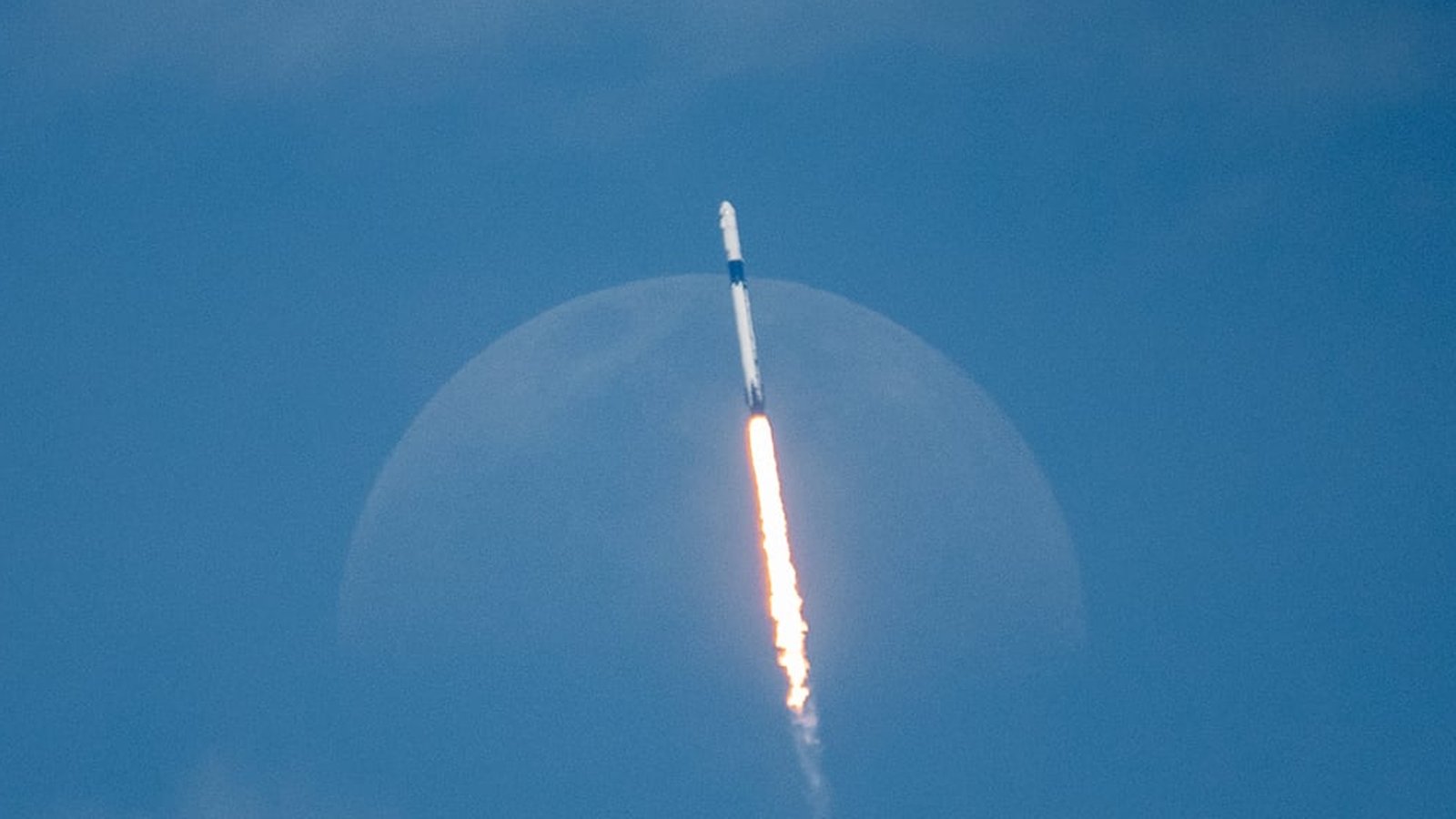 A SpaceX Falcon 9 rocket ascending into the sky in front of the moon