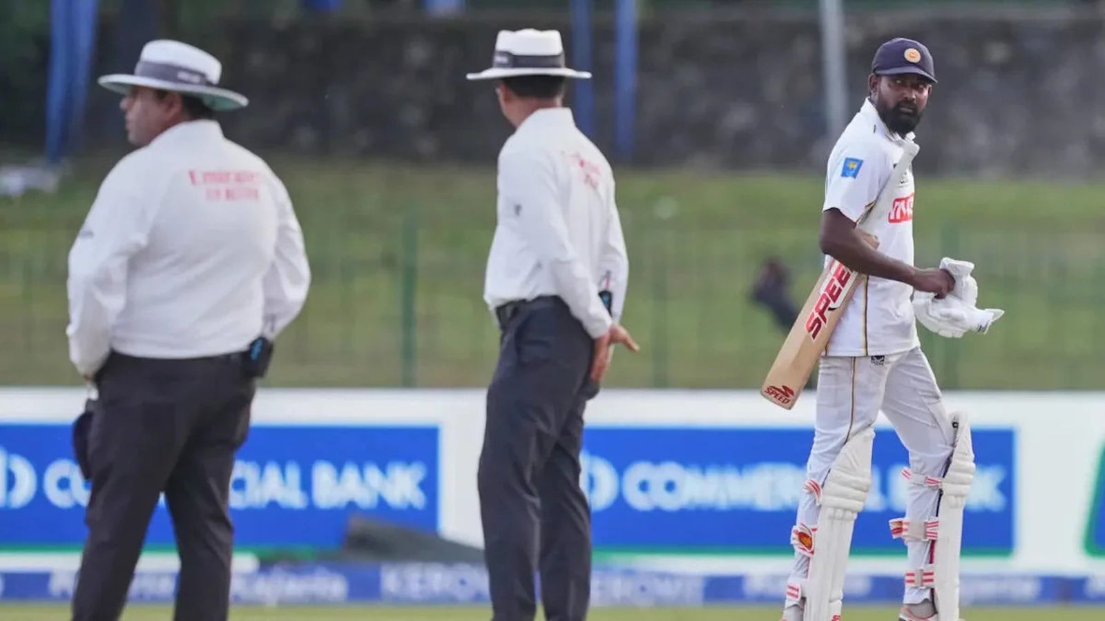 A Sri Lankan cricket batsman walks on the field past two match umpires