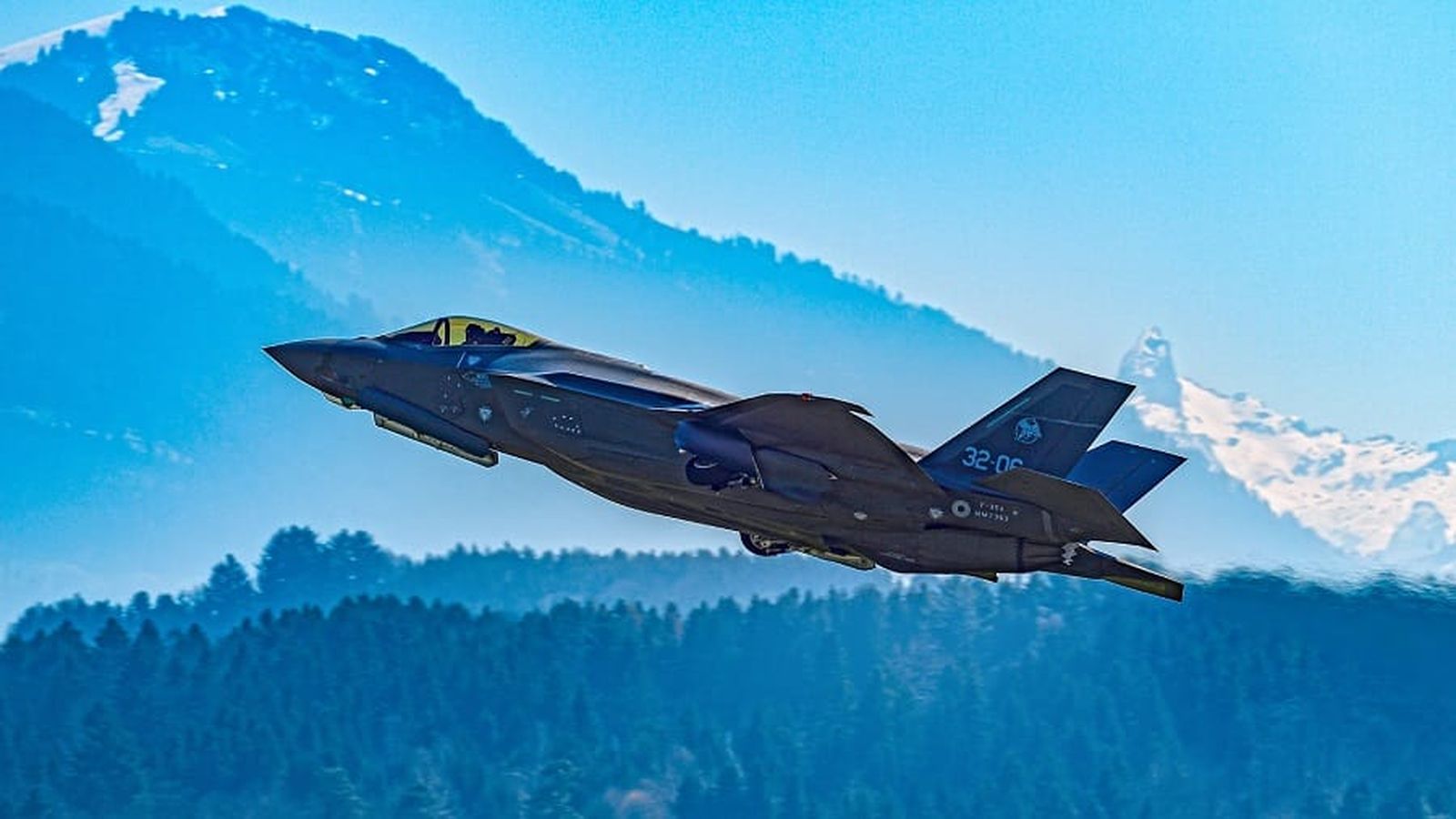 An F-35A Lightning II fighter jet flying against a backdrop of snowy mountains