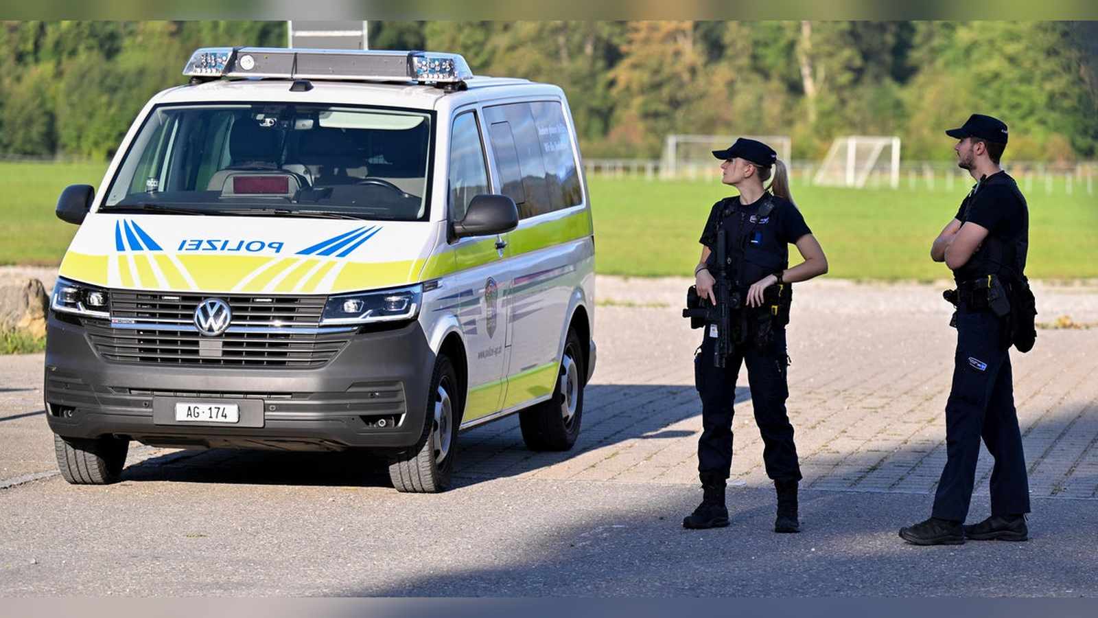 Two Swiss police officers standing near a marked police van at the shooting scene