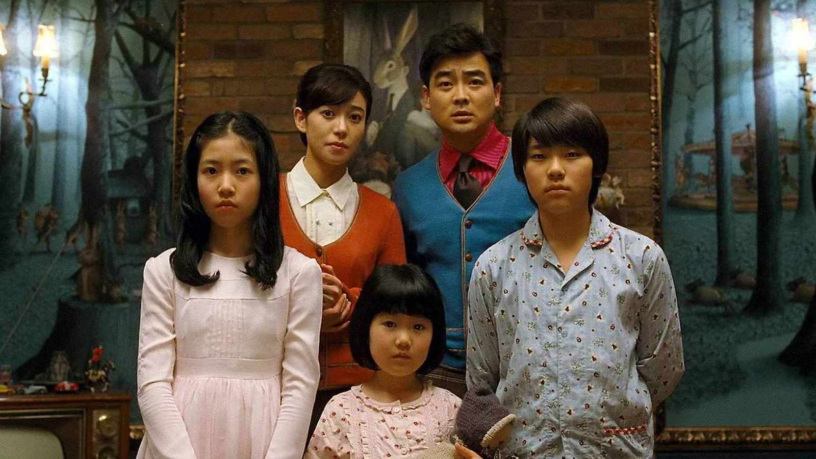 A family of five standing in a room with dark forest paintings in the background