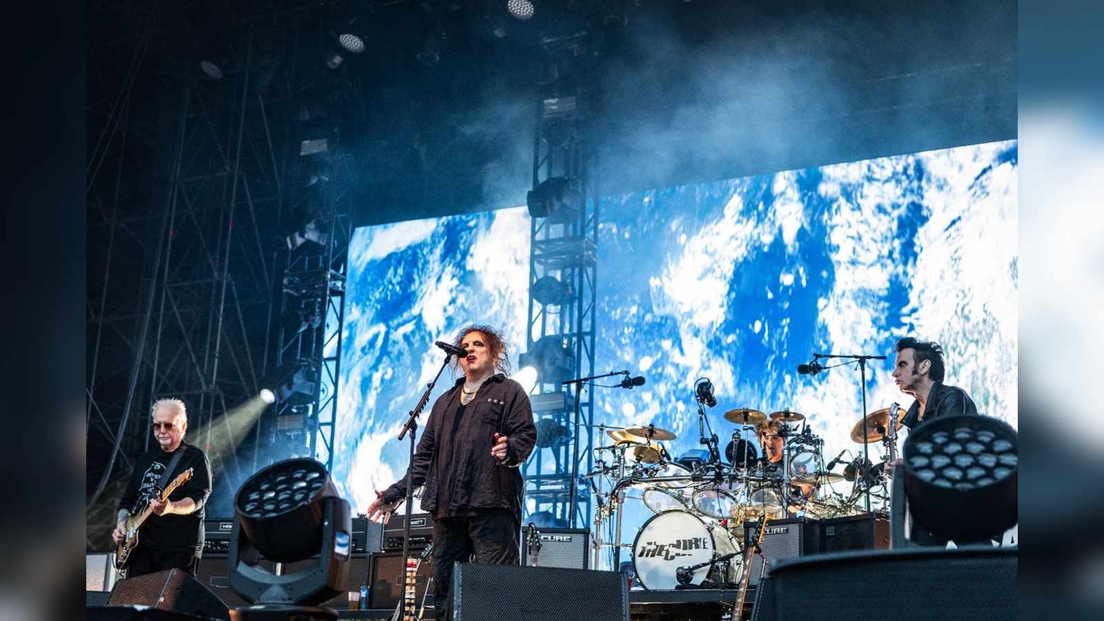 Robert Smith singing on stage with The Cure band members during a concert performance