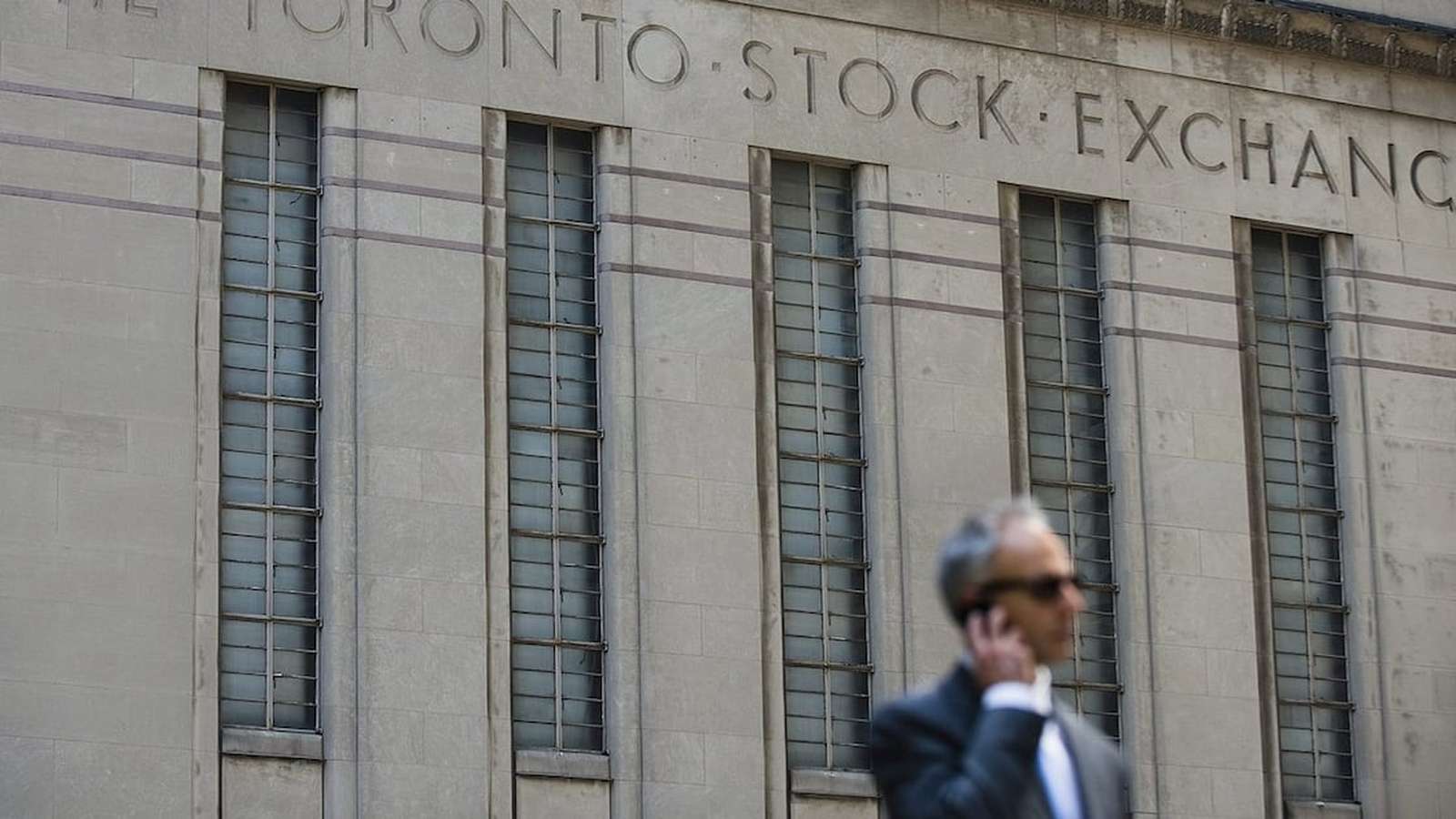 A man in a suit walks past the stone exterior of the Toronto Stock Exchange building