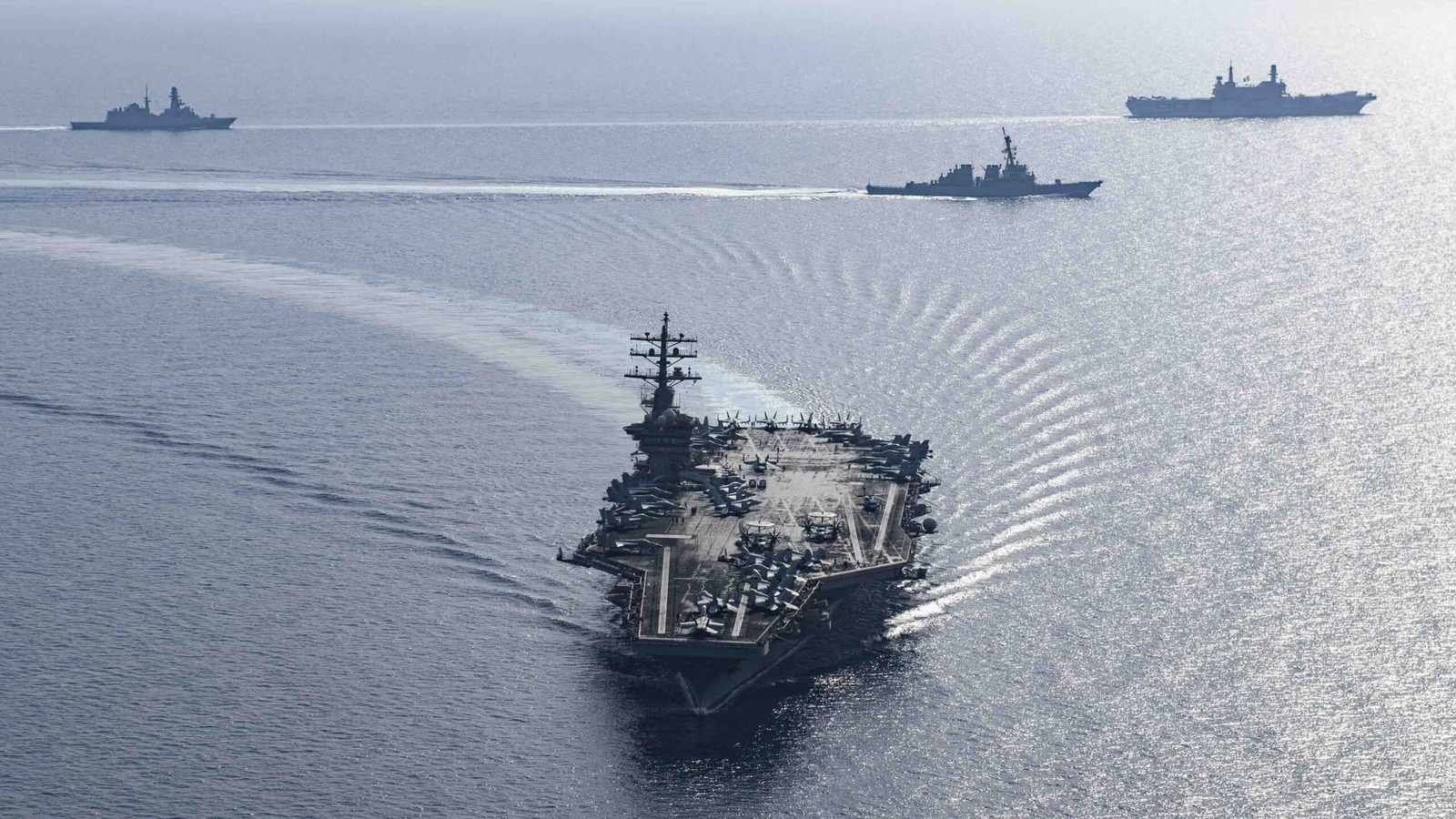 An aircraft carrier leads a naval strike group through open ocean waters