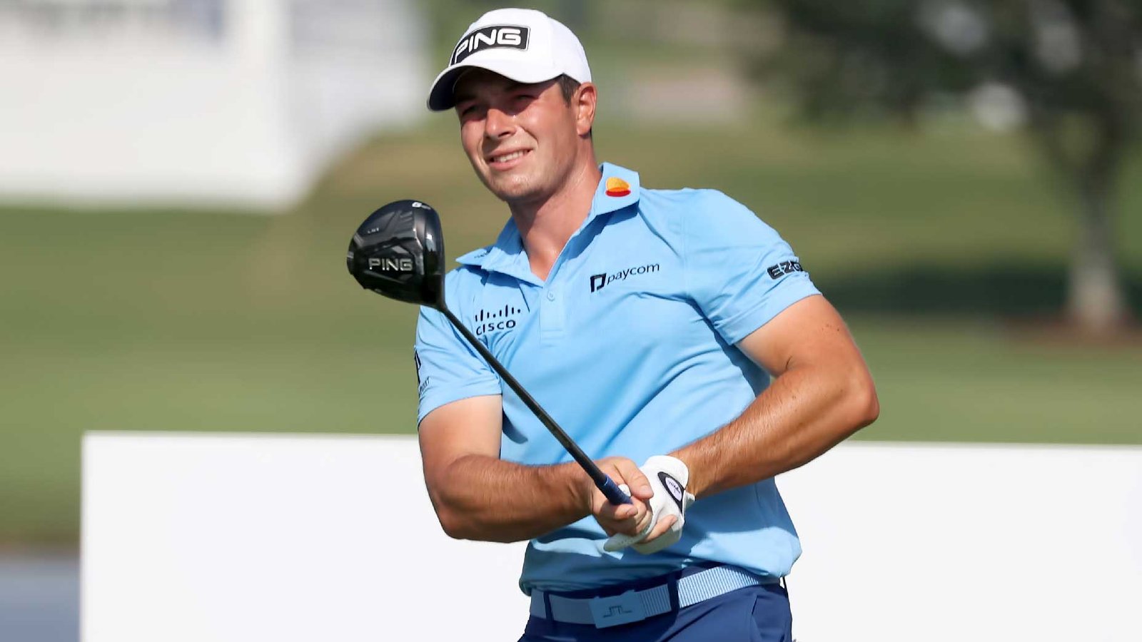Professional golfer Viktor Hovland wearing a light blue shirt and white cap swinging golf club