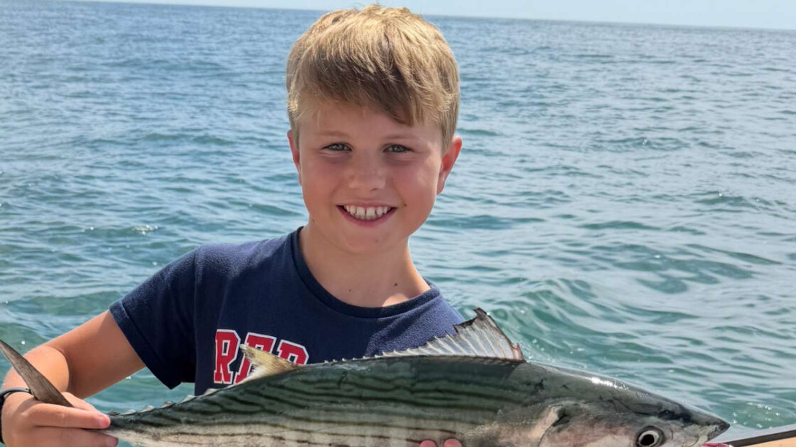 A smiling young boy holding a freshly caught fish on a boat in Nantucket