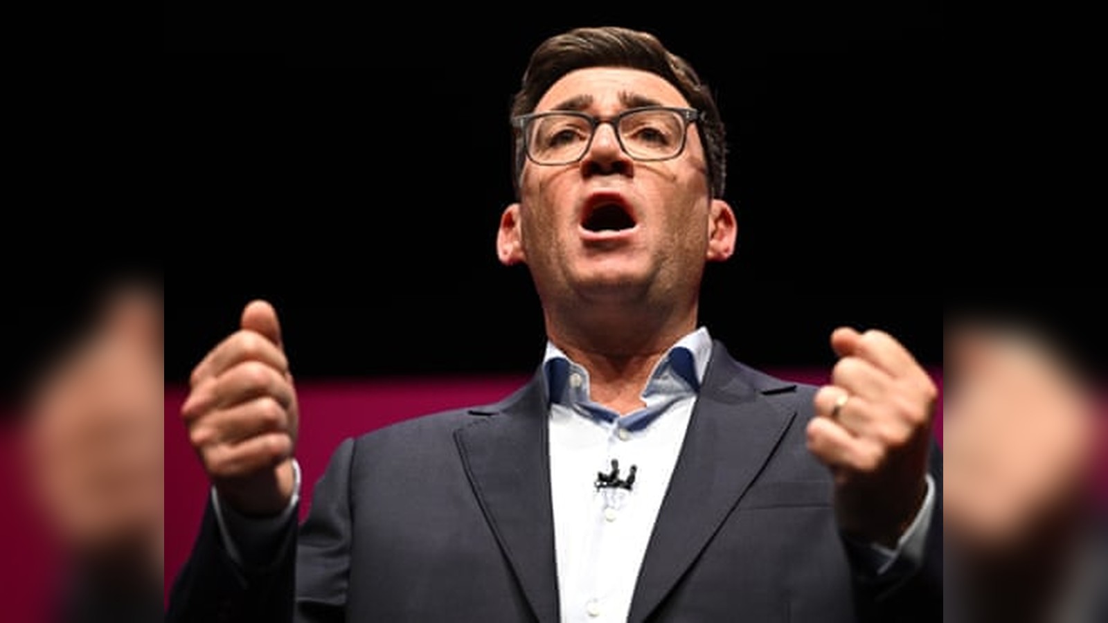 Andy Burnham wearing glasses and a suit speaking passionately with raised fists at a conference podi