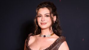 Anne Hathaway wearing a necklace and dark dress against a dark background