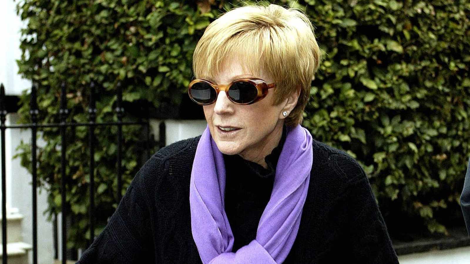 Broadcaster Anne Robinson wearing sunglasses and a purple scarf outdoors in front of greenery
