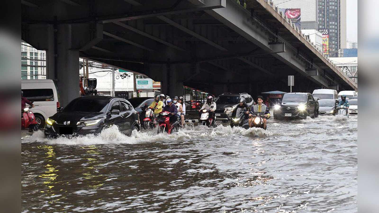 Cars and motorcycles driving through deep floodwater on a street in Bangkok, Thailand