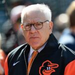 David Rubenstein wearing a black and orange Baltimore Orioles jacket at a stadium