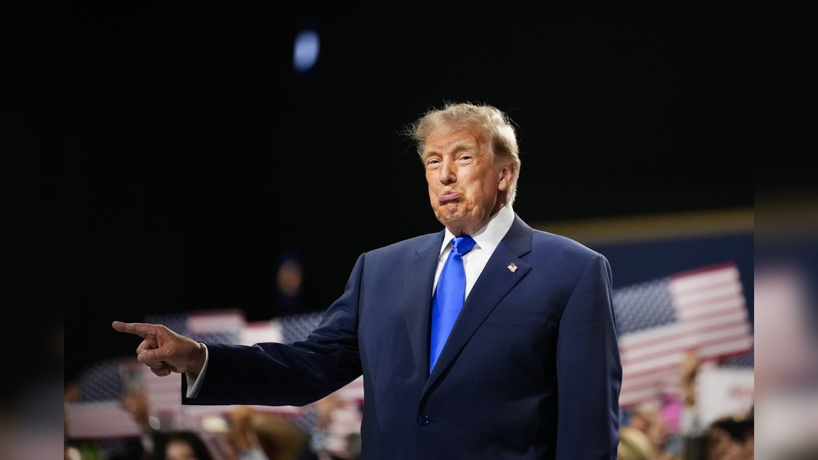 Donald Trump wearing a blue suit and tie pointing while speaking at event