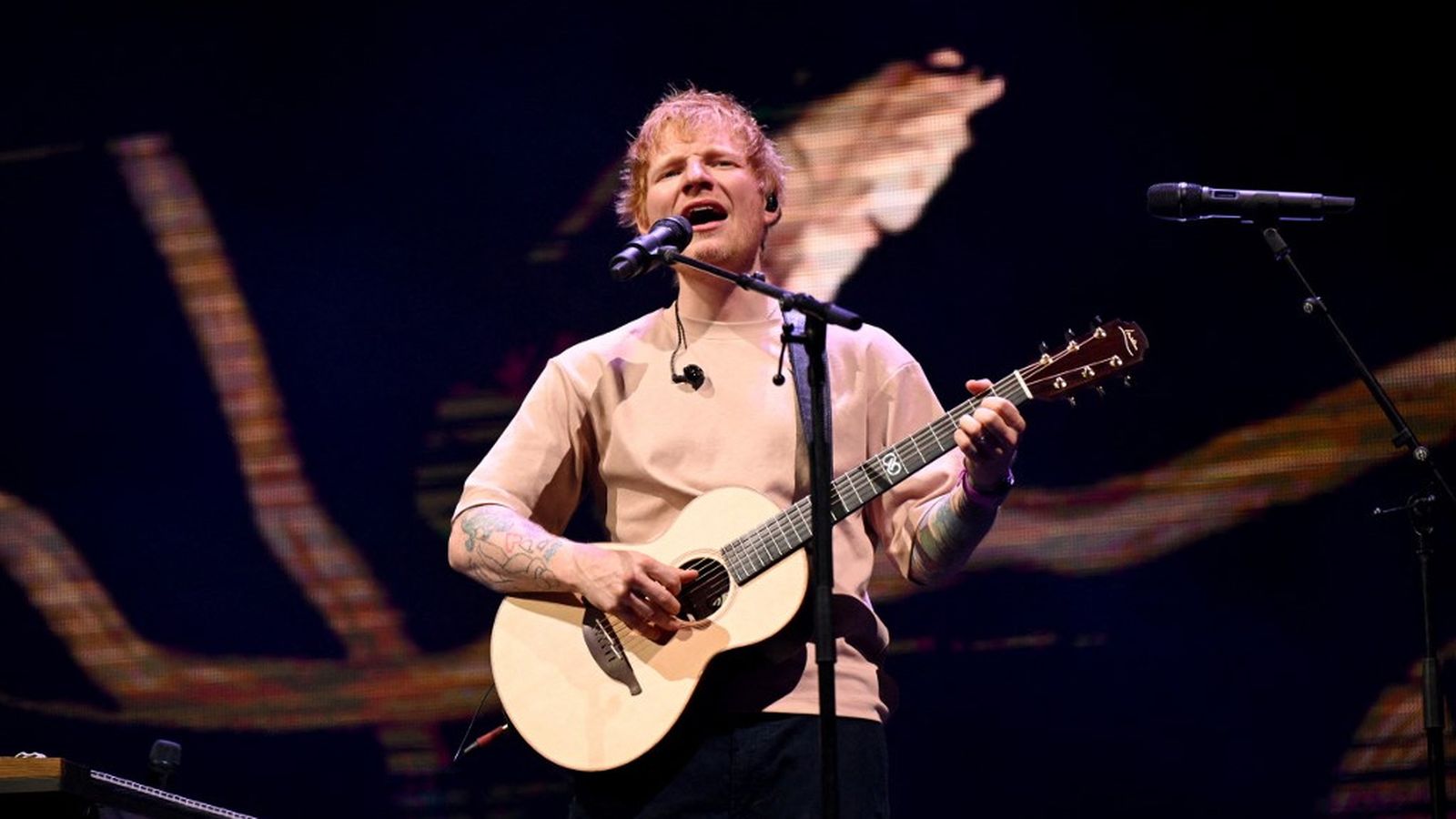 Ed Sheeran singing and playing acoustic guitar on stage during a live concert performance