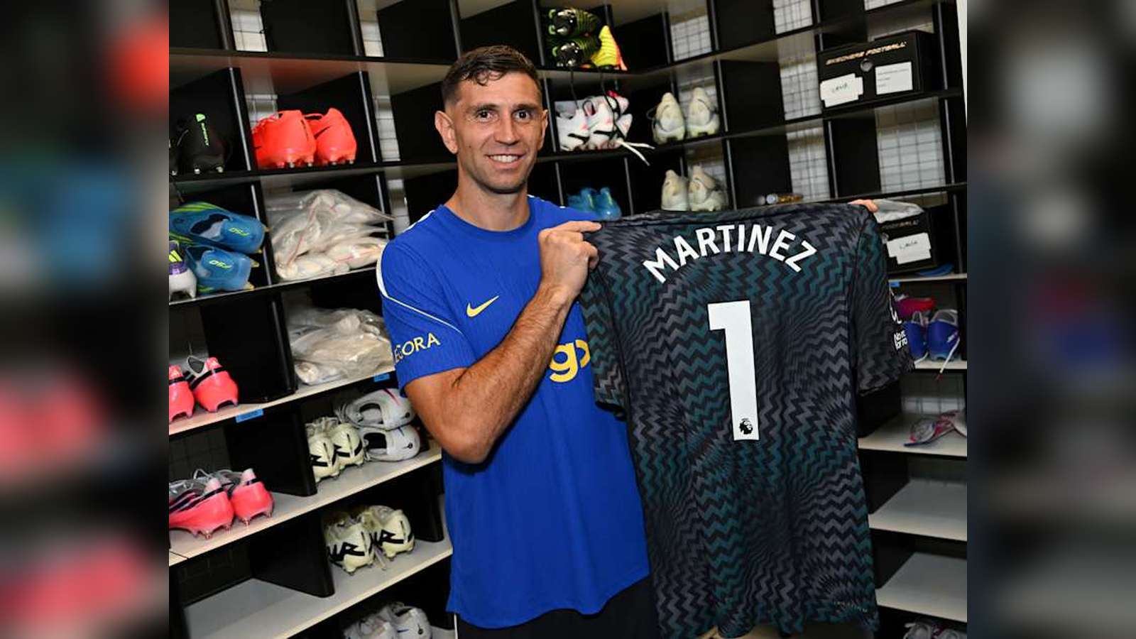 Emi Martinez smiling while holding his new Chelsea number one goalkeeper jersey
